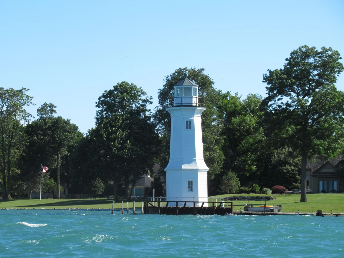 Grosse Ile North Channel Range lighthouse at the water’s edge with blue water and leafy trees