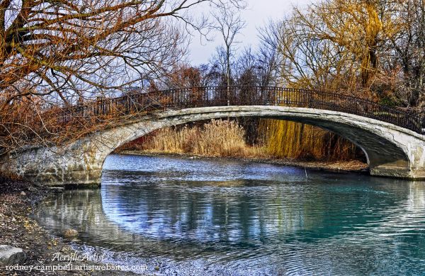 Sunlit arched bridge over blue-green water with golden trees at Elizabeth Park in Trenton
